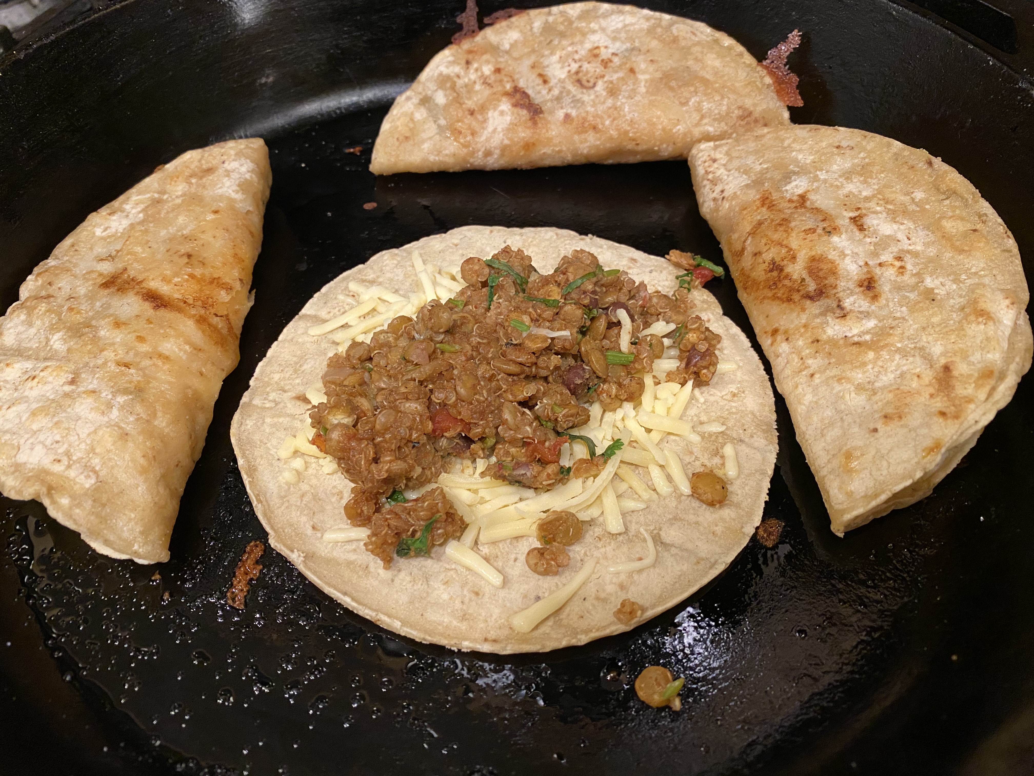 A corn tortilla frying in a cast iron pan, topped with melted Chihuahua cheese and lentil taco meat filling.